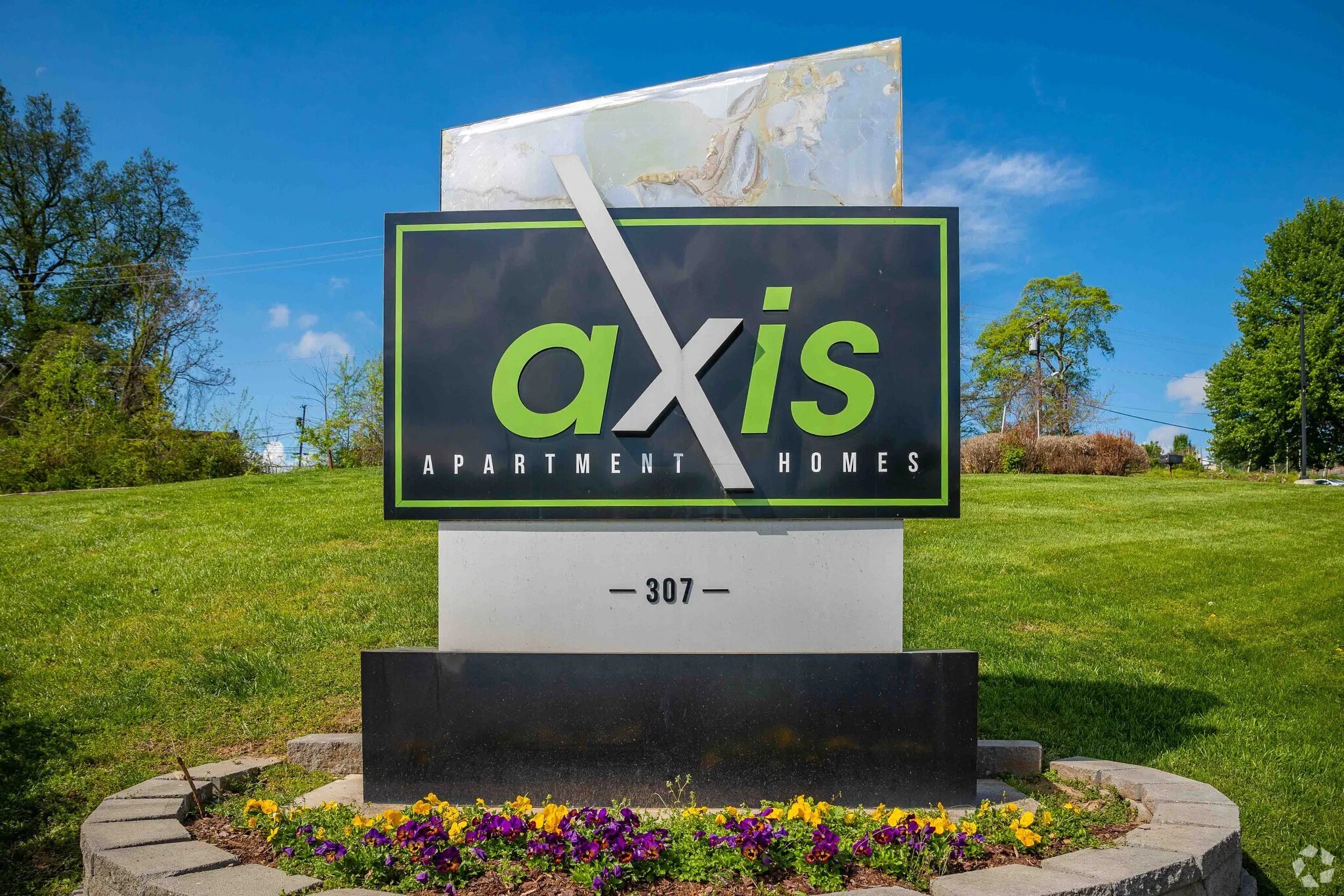 A sign for Axis Apartment Homes is displayed in a garden.